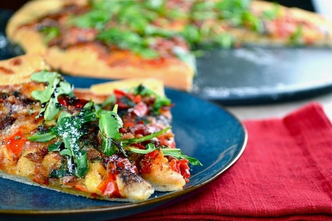 Crispy veggie pizza with fresh greens on dark plate, close-up, delicious baked pizza with colorful toppings and melted cheese, perfect for pizza lovers and family dinners, from Stuck On Sweet.