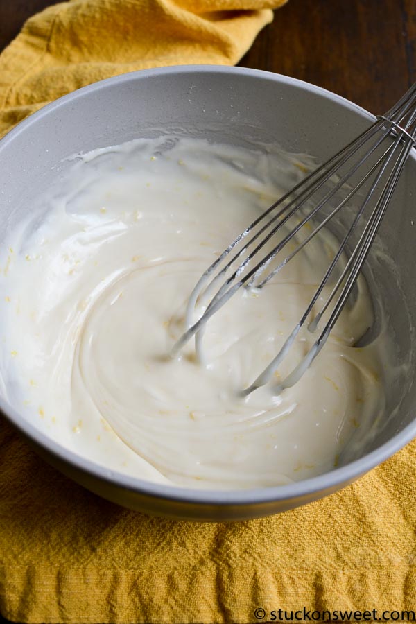 Creamy vanilla frosting in a mixing bowl with a whisk, perfect for cake decoration and sweet desserts.