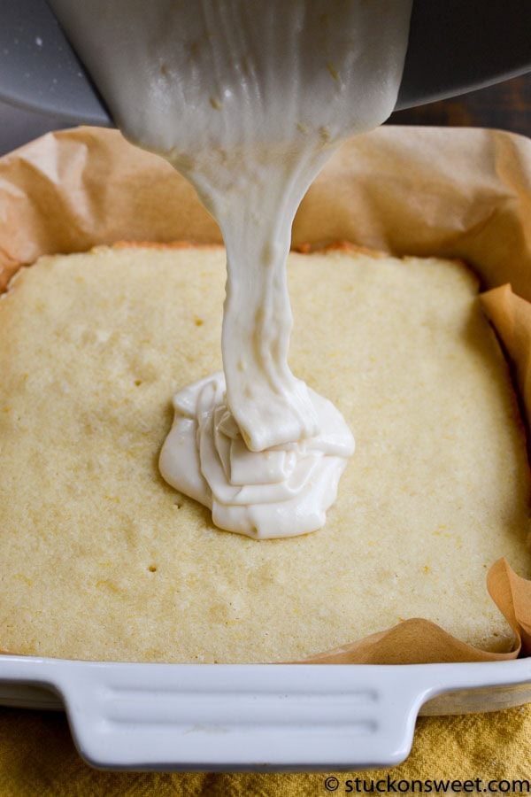 Golden sponge cake batter in a baking pan with creamy cake icing pouring over it.