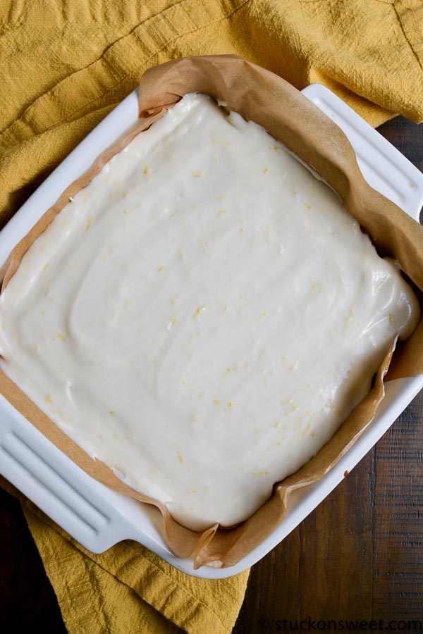 Cream cheese layered cake batter in a baking dish, ready to be baked, with parchment paper lining, on a dark wooden surface with a mustard-colored cloth.