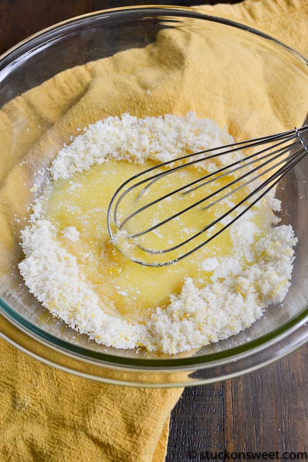 Buttery yellow cake batter with flour and melted butter in a glass mixing bowl, whisk ready for baking, on a wooden surface with a yellow cloth, for delicious homemade cake recipes.