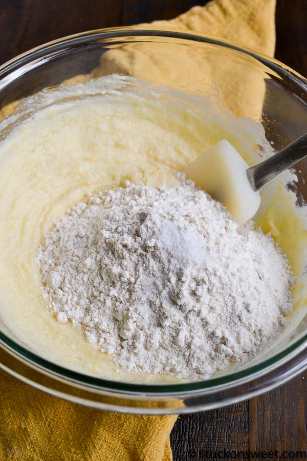 Flour being added to yellow cake batter in a glass mixing bowl.