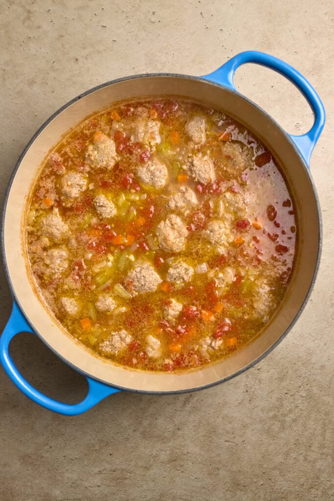 Savory homemade meatball and vegetable soup in a blue Dutch oven, bubbling with broth and colorful ingredients, perfect for comforting and hearty meals.