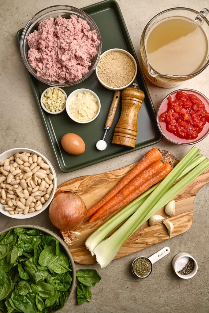 Creamy white beans, diced onion, carrots, celery, garlic, herbs, and vegetable broth arranged on a kitchen countertop for a flavorful healthy turkey meatball soup recipe.
