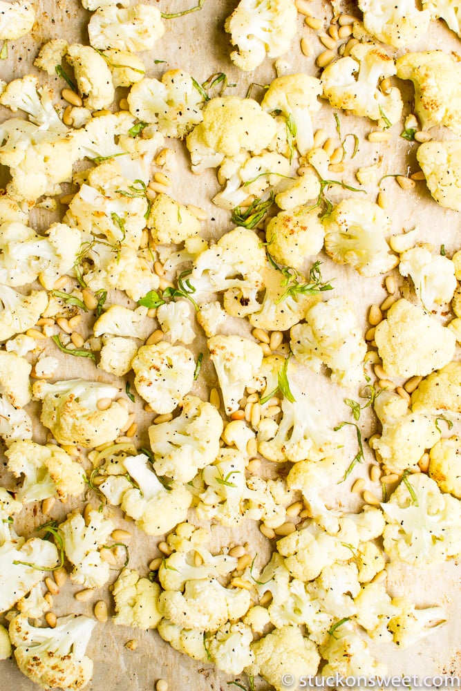 Roasted cauliflower florets with pine nuts and fresh herbs on parchment paper.