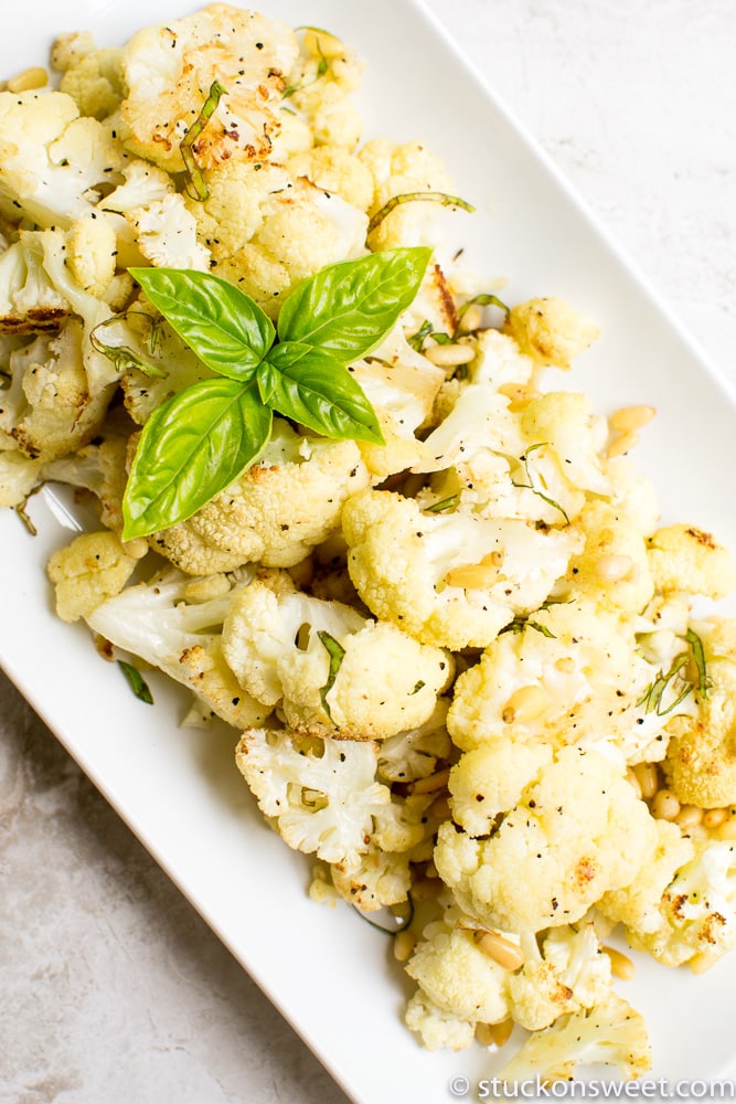 Roasted cauliflower with herbs and pine nuts on a white serving platter.