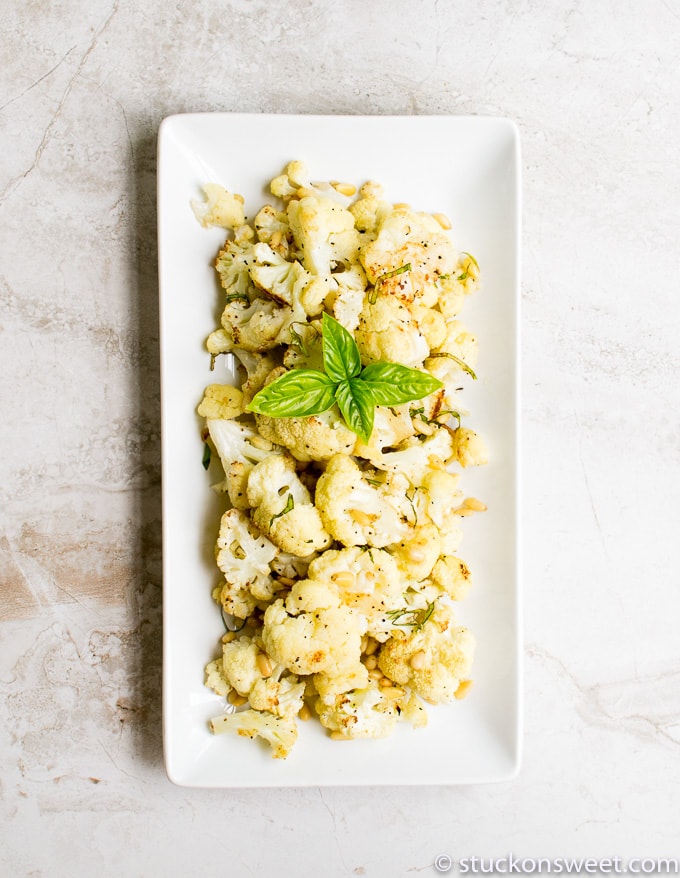 Crispy roasted cauliflower florets garnished with basil on a white rectangular plate, perfect for a healthy snack or side dish.