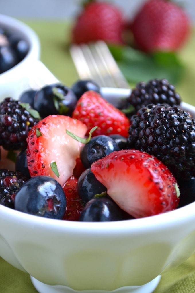 Fresh mixed berries including strawberries, blueberries, blackberries, and raspberries in a white bowl, perfect for healthy snacking or dessert.