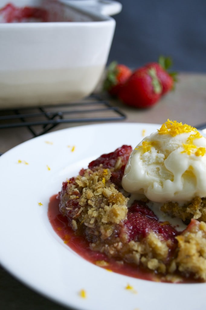 Fresh strawberry crumble pie topped with vanilla ice cream and lemon zest on a white plate, showcasing sweet and fruity dessert options with a golden crumb topping.