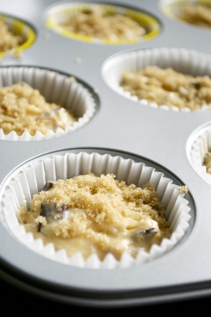 Softened cookie dough topped with brown sugar and chocolate chips in a muffin tin for baking cookies.