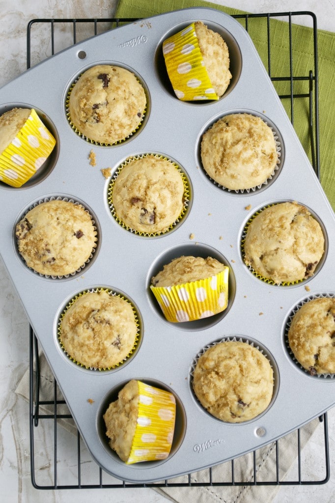 Fluffy banana muffins with chocolate chips in a muffin tin, some wrapped in colorful polka-dot cupcake liners.