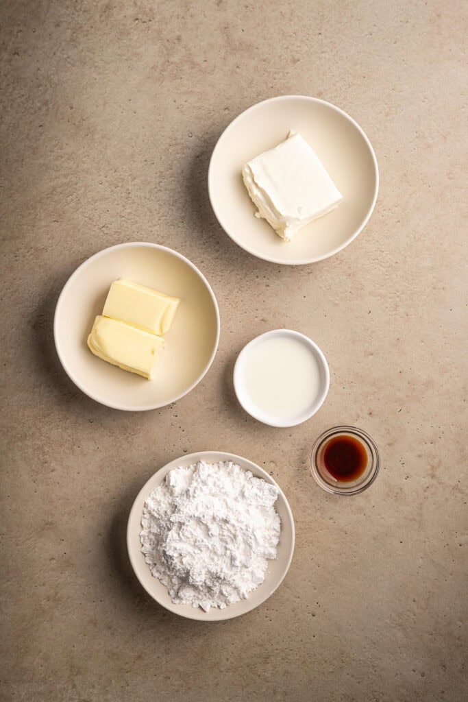 Cream cheese and butter squares with vanilla extract, milk, and powdered sugar for cheesecake recipe.