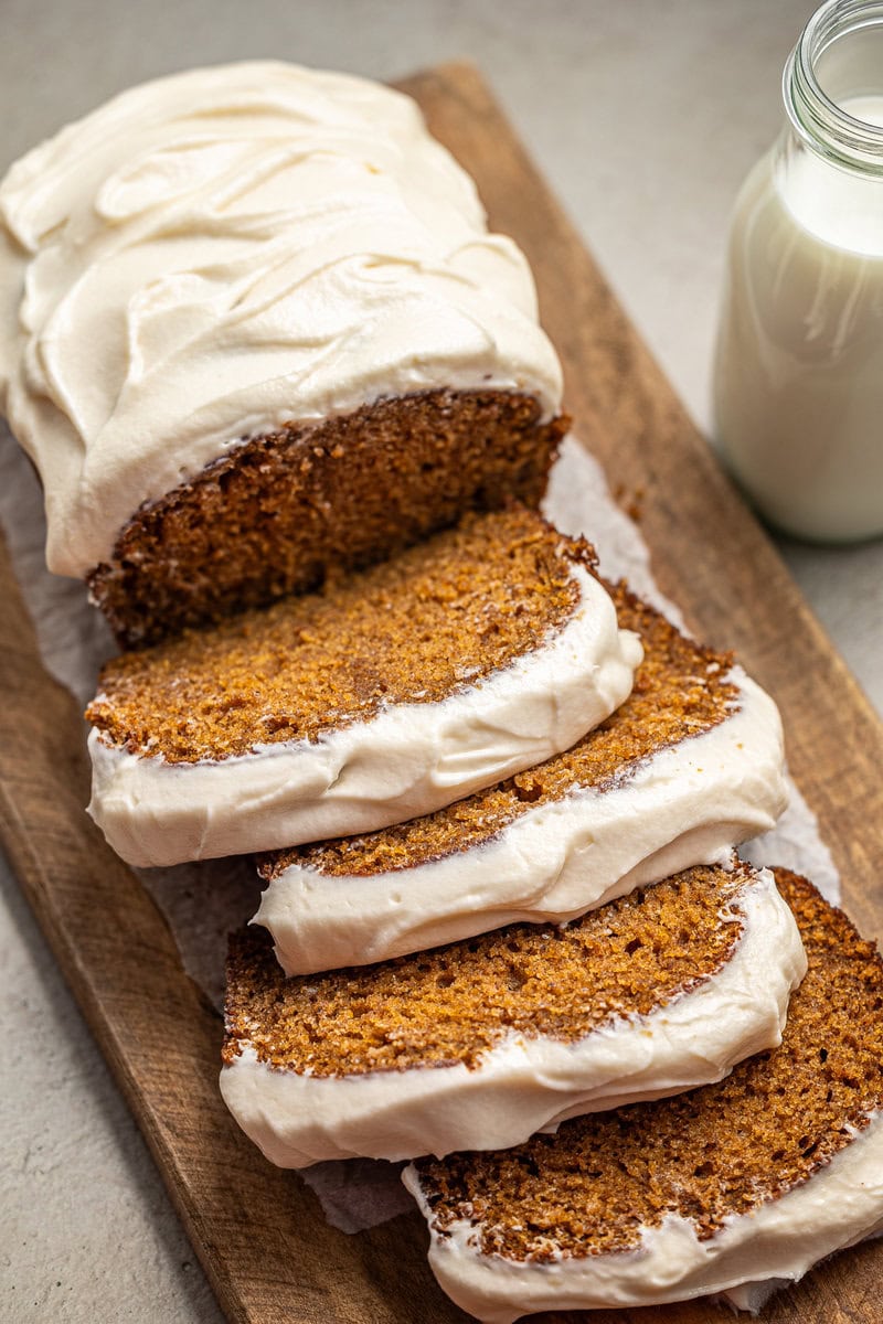 Cream cheese carrot cake with frosting, sliced to reveal moist texture and spiced flavor, served on wooden board with glass of milk. Perfect for dessert or special occasions.