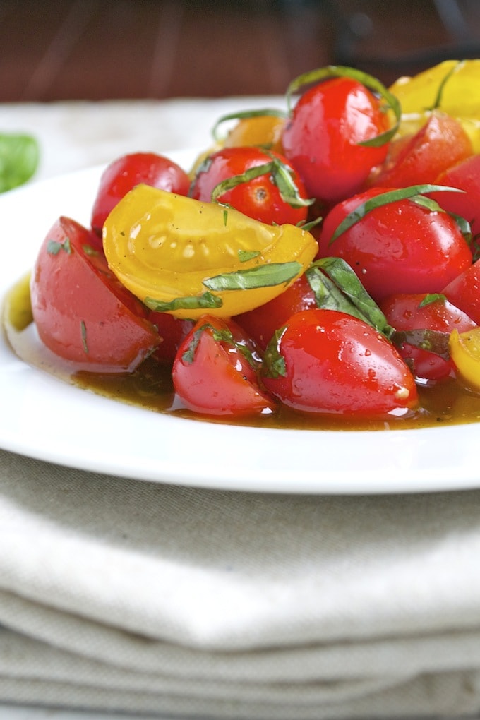 Bright cherry tomatoes with fresh basil on a white plate, drizzled with balsamic glaze, showcasing a vibrant and flavorful Italian-inspired appetizer or salad recipe.