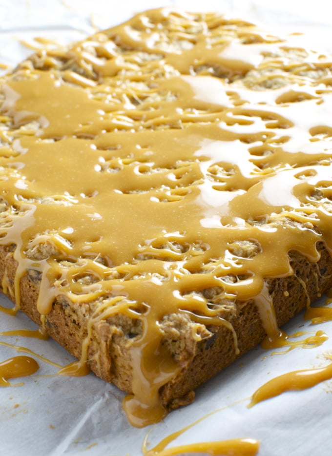 Chewy caramel cookie bar drizzled with caramel sauce and white icing, golden-brown edges, close-up on parchment paper. Perfect dessert for caramel lovers and sweet snack enthusiasts.
