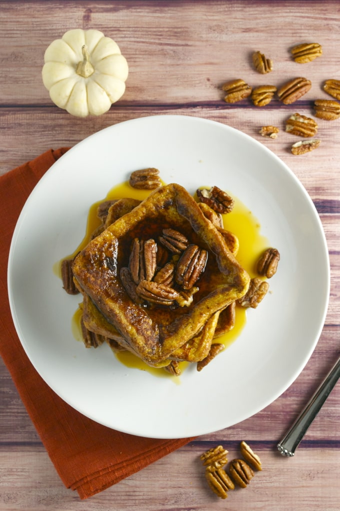 Creamy French toast casserole topped with pecans and drizzled with syrup on a white plate. Perfect for breakfast or brunch, combining sweet flavors and crispy textures.