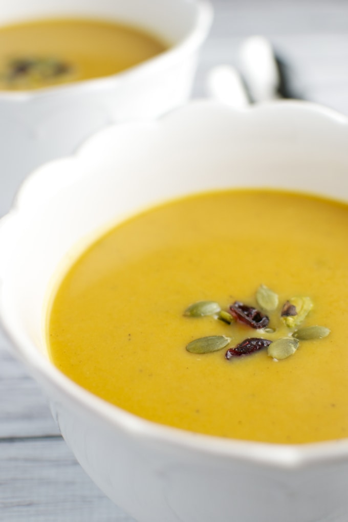 Creamy pumpkin soup garnished with pumpkin seeds and dried cranberries in white bowls, perfect for fall or winter comfort food. Healthy, delicious, and easy to prepare.