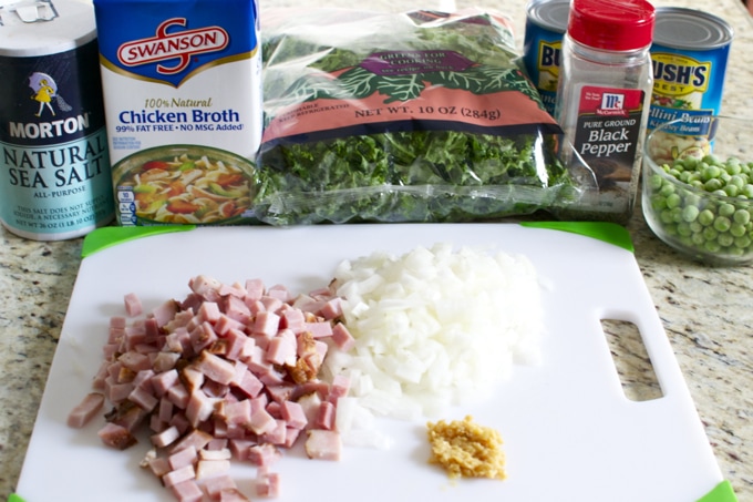 Diced ham, chopped onions, garlic, and fresh greens on a cutting board with ingredients for soup or salad.