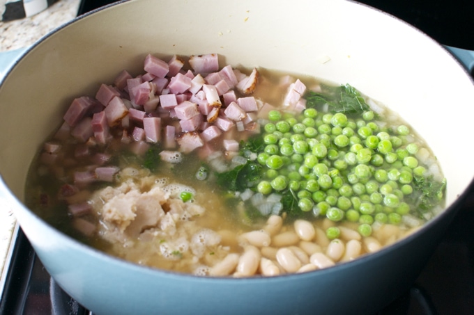 Cooked chicken, white beans, green peas, and chopped ham simmering in a pot for a hearty stew - perfect comfort food.