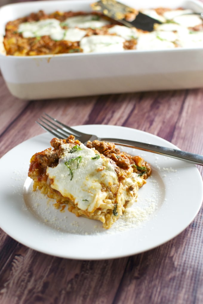 Cheeseburger casserole with melted cheese and ground beef served on a white plate, close-up, with a baking dish in the background.