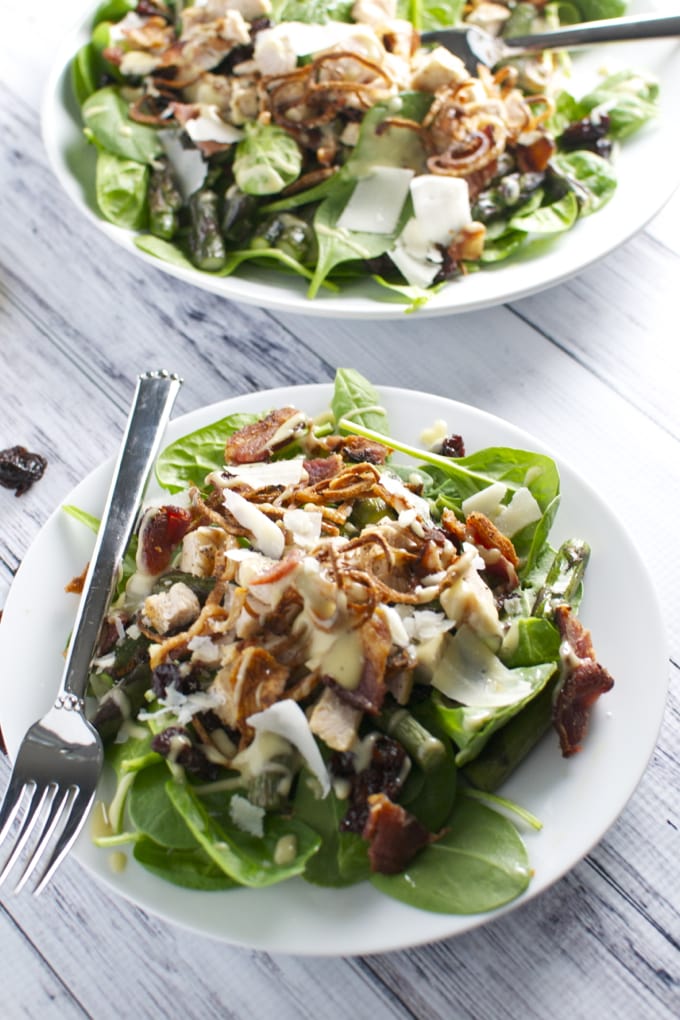 Fresh spinach salad with grilled chicken, bacon, shredded cheese, and balsamic glaze on white ceramic plates. Healthy and delicious meal option.