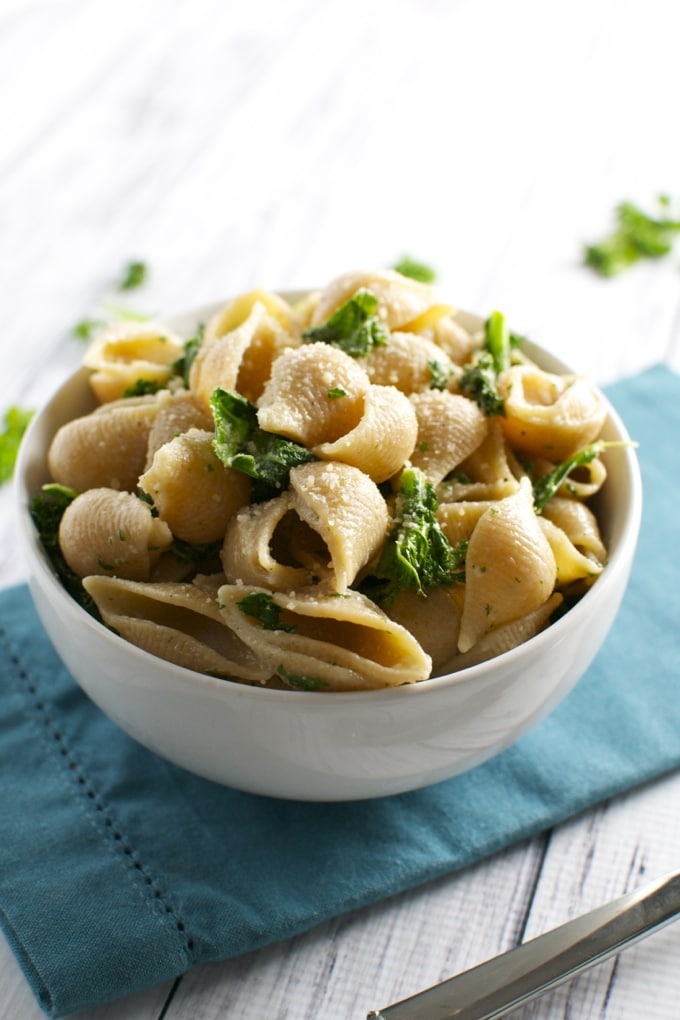 Creamy pasta with fresh herbs and grated cheese in a white bowl on a blue napkin.