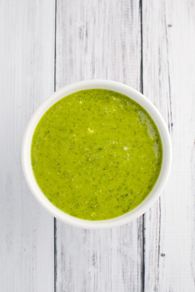Creamy green pesto sauce in a white bowl on a rustic white wooden surface.