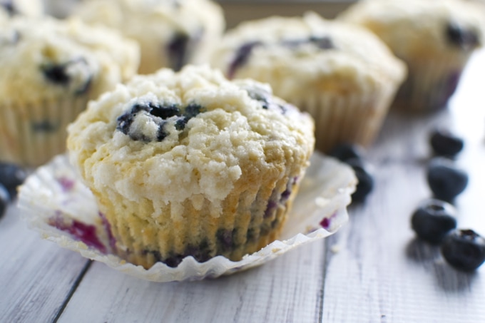Fresh blueberry muffins on a rustic wooden surface with scattered blueberries, showcasing homemade bakery quality and delicious, moist blueberry flavor.