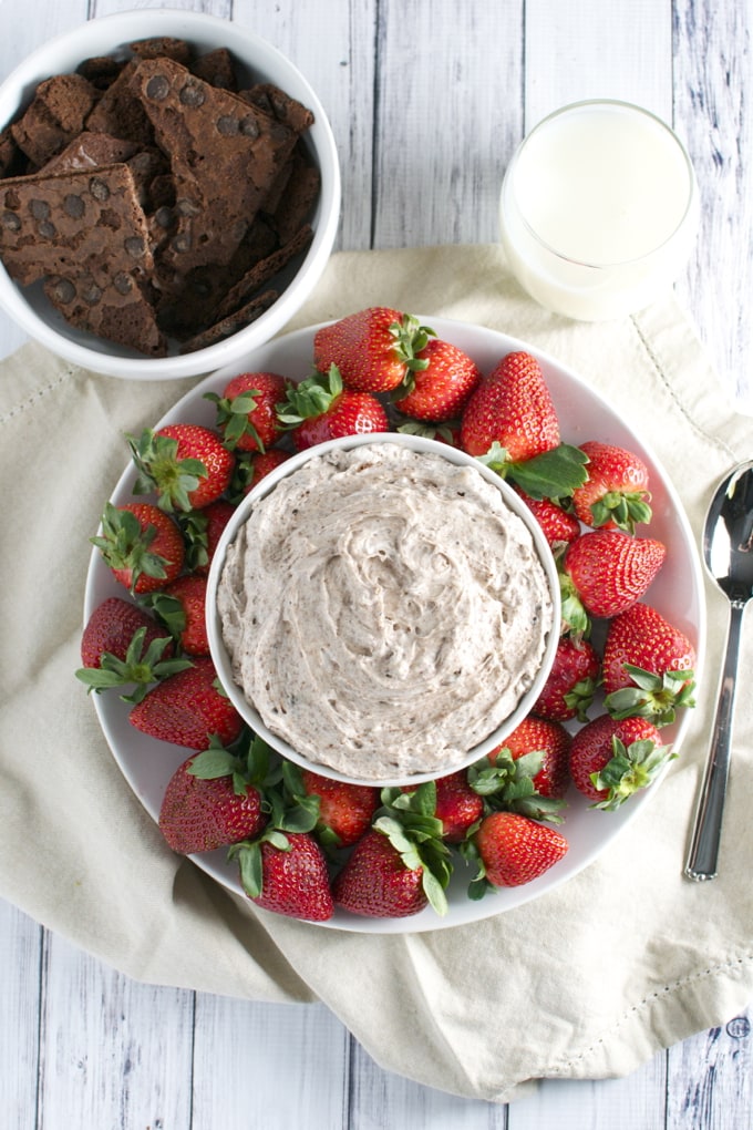 Creamy chocolate chip fudge surrounded by fresh strawberries and a glass of milk on rustic wooden background. Perfect for homemade dessert recipes or sweet snack ideas.