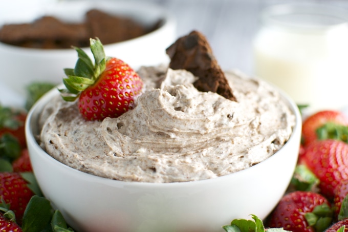 Rich, creamy chocolate frosting with fresh strawberries and chocolate chunks in a white bowl on a colorful dessert platter.