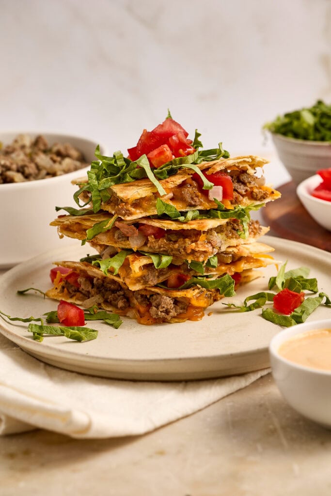 Delicious cheeseburger quesadillas stacked with melted cheese, ground beef, fresh lettuce, and tomatoes, served with side dips for a flavorful meal.