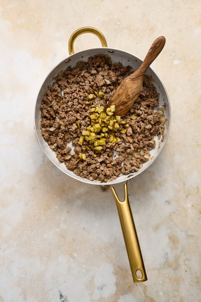 Cooked ground beef with diced pickles in a skillet, ready to be used as filling for cheeseburger quesadillas.
