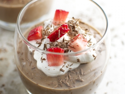 Rich chocolate pudding topped with whipped cream, fresh strawberries, and chocolate shavings, served in a clear glass – perfect for dessert lovers.