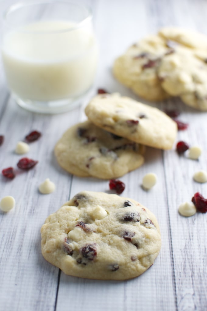 Buttery cranberry white chocolate chip cookies on a rustic white wooden table with a glass of milk. Perfect for holiday baking and festive treats. Freshly baked, chewy, and filled with white chocolate and tart cranberries.
