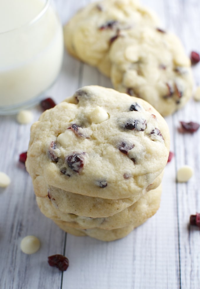 Creamy white chocolate cranberry cookies stacked with a glass of milk in the background. Perfect for dessert or holiday treats, featuring fresh cranberries and white chocolate chips.