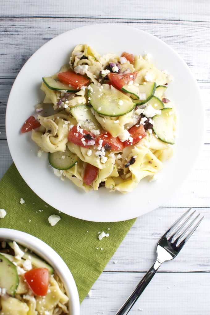 Creamy vegetable tortellini pasta with fresh zucchini, tomatoes, and feta cheese on a white plate, served with a fork. Perfect for a flavorful and easy-to-make meal.