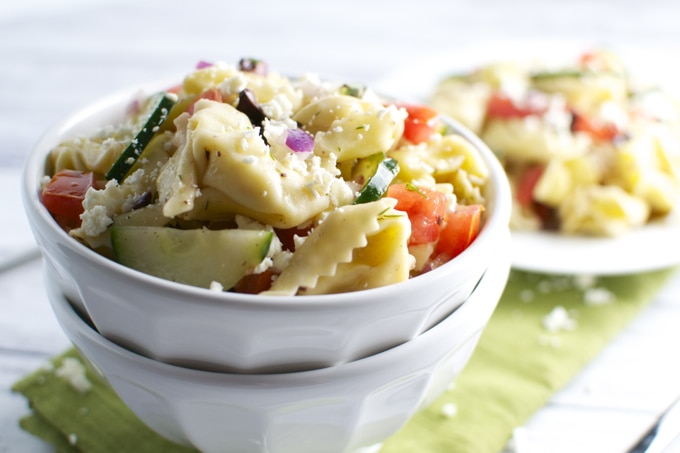 Fresh veggie pasta salad with cheese, tomatoes, cucumbers, and herbs in a white bowl, served as a healthy, delicious summer side dish. Perfect for picnics and outdoor gatherings.