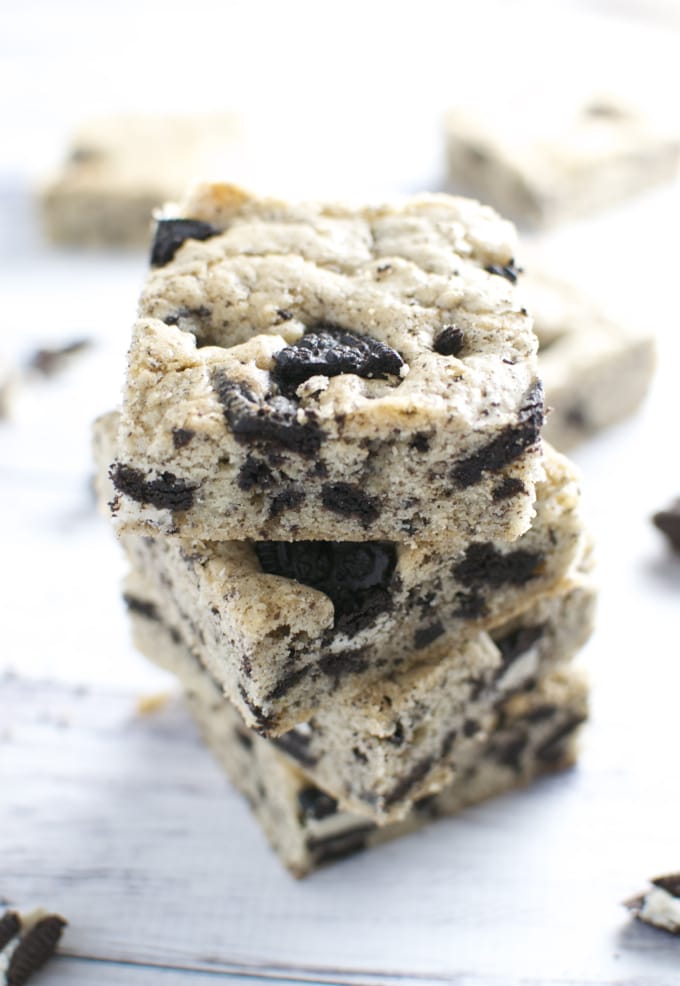 Oreo cookie brownies stacked on white wooden surface, showing crumbly texture and chocolate chips, delicious dessert suitable for cookie lovers and baked goods enthusiasts.