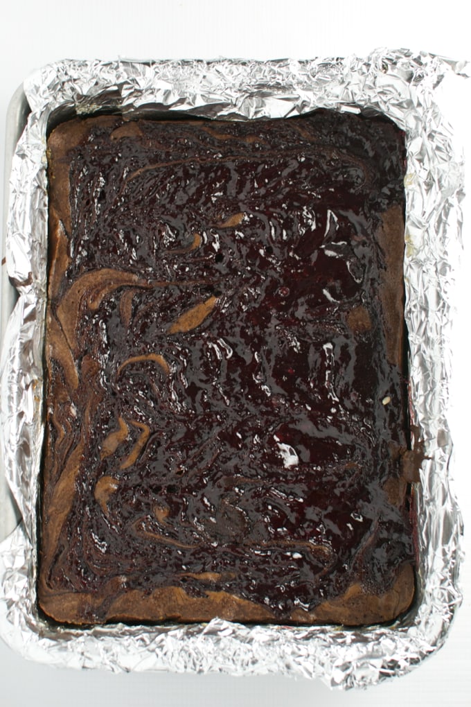Rich chocolate brownie with swirls of caramel and glossy chocolate glaze topped with shiny chocolate drizzle in a baking tray.