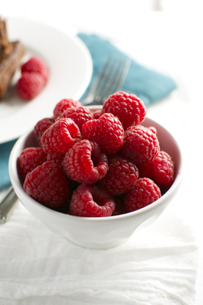 Fresh raspberries in a white bowl, perfect for desserts or snacking.