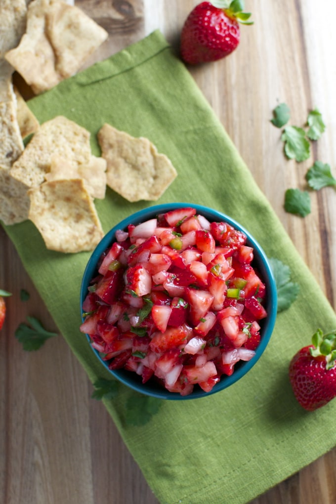 Fresh strawberry salsa with crunchy chips on a rustic wooden table, perfect for summer snacks or parties. Made with diced strawberries, onions, and herbs for a sweet and savory flavor.