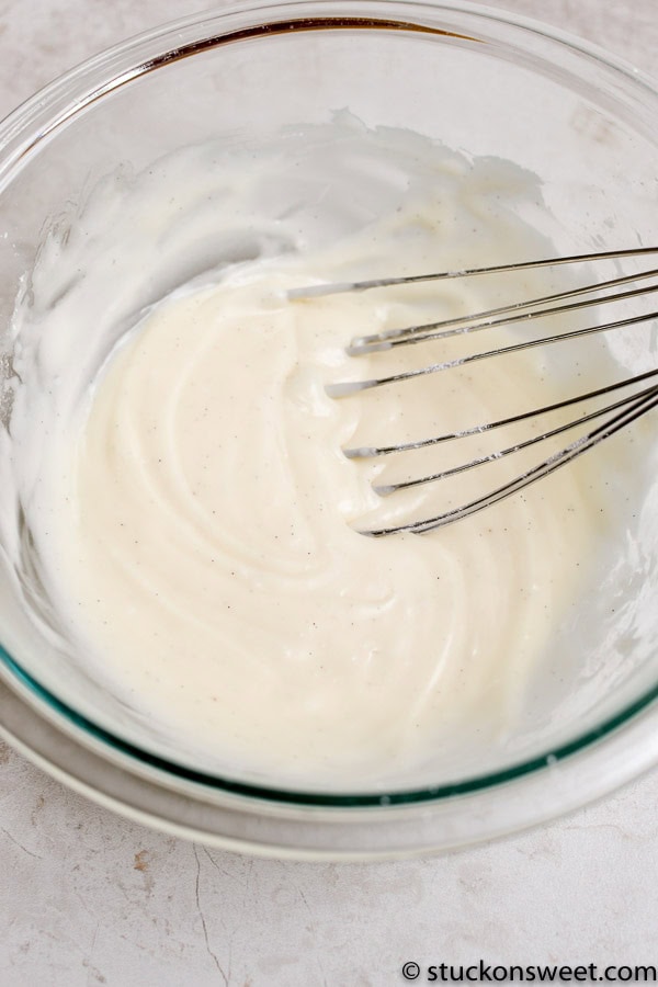 Creamy homemade vanilla frosting in a glass mixing bowl with a whisk for baking or decorating sweets. Perfect for cakes, cupcakes, and desserts.