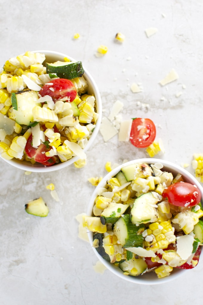 Fresh corn salad with cherry tomatoes, cucumbers, and shredded cheese in white bowls, served as a delicious side dish. Perfect for summer meals, easy to make, and full of fresh flavors.
