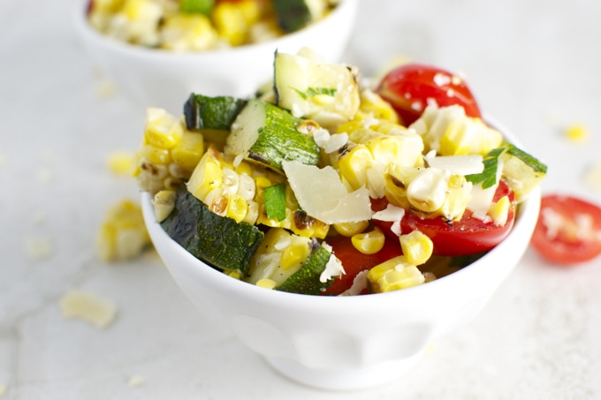 Juicy cherry tomatoes, fresh zucchini, corn, and cheese salad served in a white bowl, healthy vegetarian dish, vibrant summer vegetable salad, perfect for a light meal or side dish.
