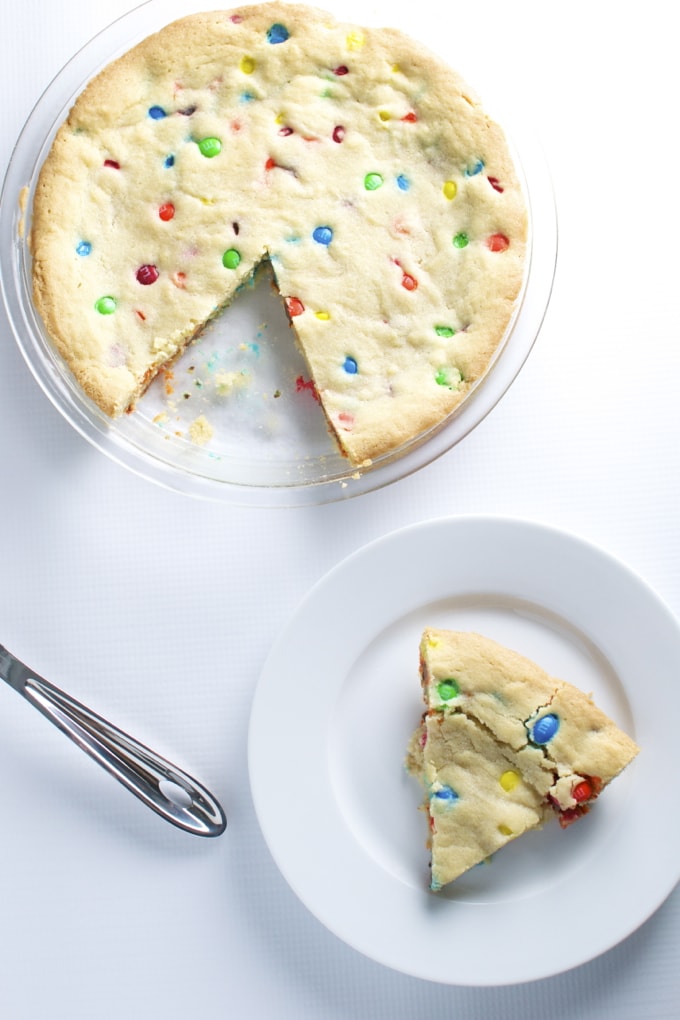 Colorful sprinkle sugar cookie cake with a slice on a white plate, perfect for parties and celebrations at Stuck On Sweet.