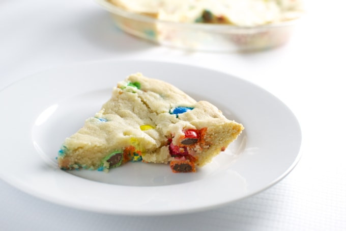 Colorful candy cookie on white plate with gift bowl in the background, perfect for sweet tooth cravings and dessert lovers.