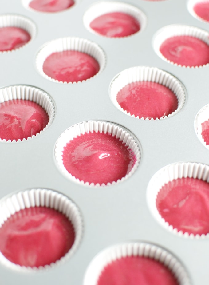 Bright pink frosting in cupcake liners in a baking tray, ready for decoration or baking.