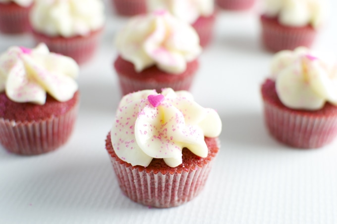 Red velvet cupcakes with white frosting and pink sprinkles, perfect for Valentine's Day or special occasions.