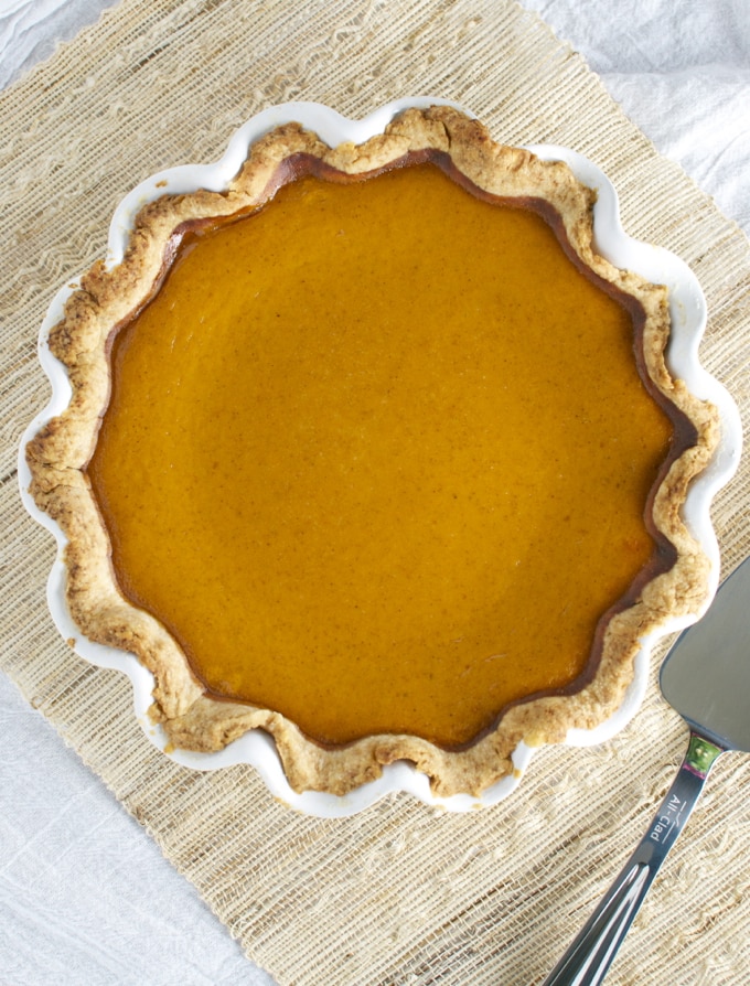 Golden pumpkin pie with a flaky crust on a textured cloth surface, ready to serve. Perfect for fall holidays and dessert cravings, showcasing classic homemade pie recipes.