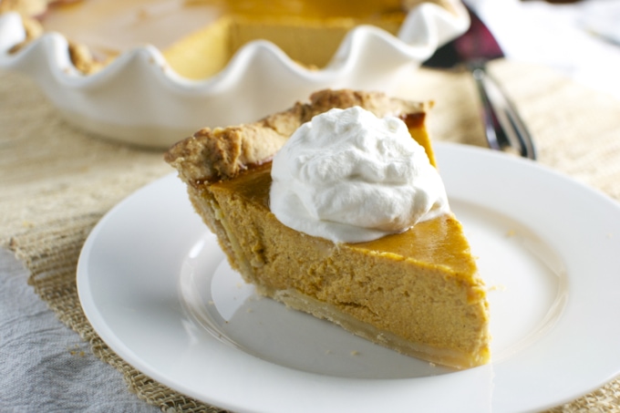 Rich pumpkin pie slice with whipped cream topping, served on a white plate at Stuck On Sweet bakery.